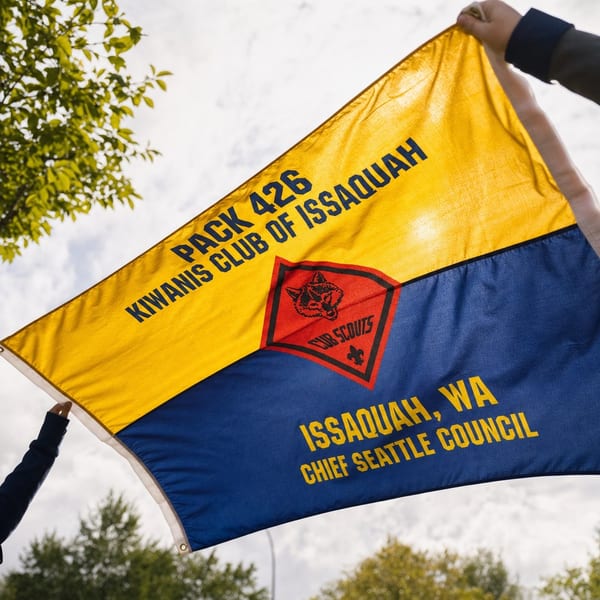 The Pack 426 flag held open against a bright sky, gold above and blue below, with the Cub Scouts wolf-head diamond at its centre.